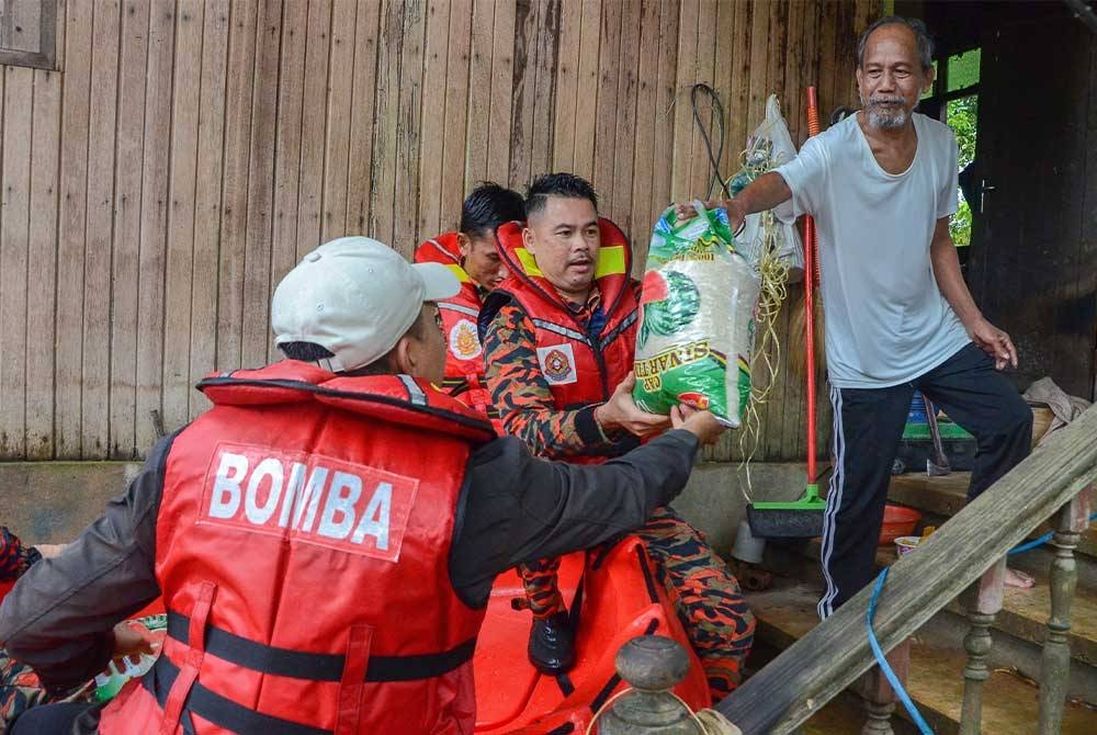 Anggota Bomba dan Penyelamat Rantau Panjang membantu Badan Bukan Kerajaan Yayasan Raja Shamri (YRS) menyampaikan bantuan barangan keperluan asas kepada salah seorang penduduk Kampung Padan Licin yang terjejas akibat bencana banjir sejak seminggu lalu. - Foto Bernama