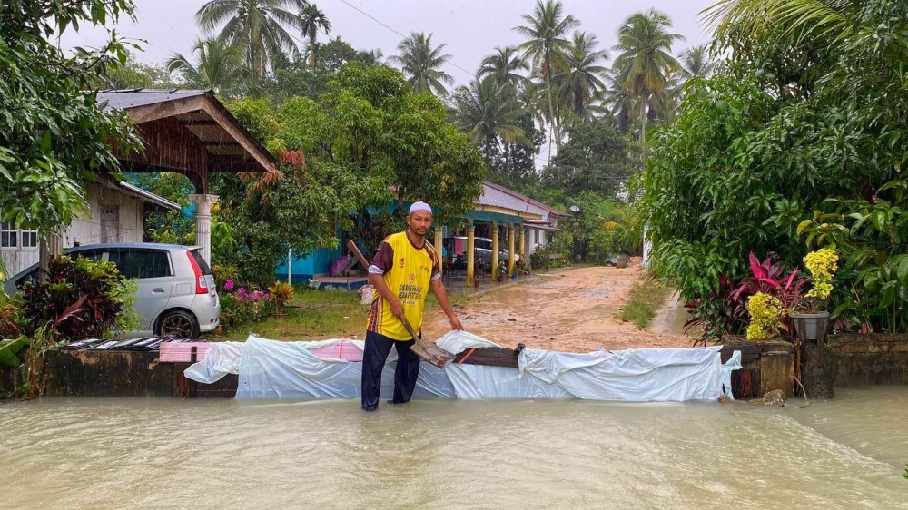 Suhaimi menggunakan plastik sebagai benteng bagi mengelak limpahan air memasuki kawasan kediaman mereka di Kampung Banggol Tiga Daerah, Bukit Abal, Pasir Puteh.