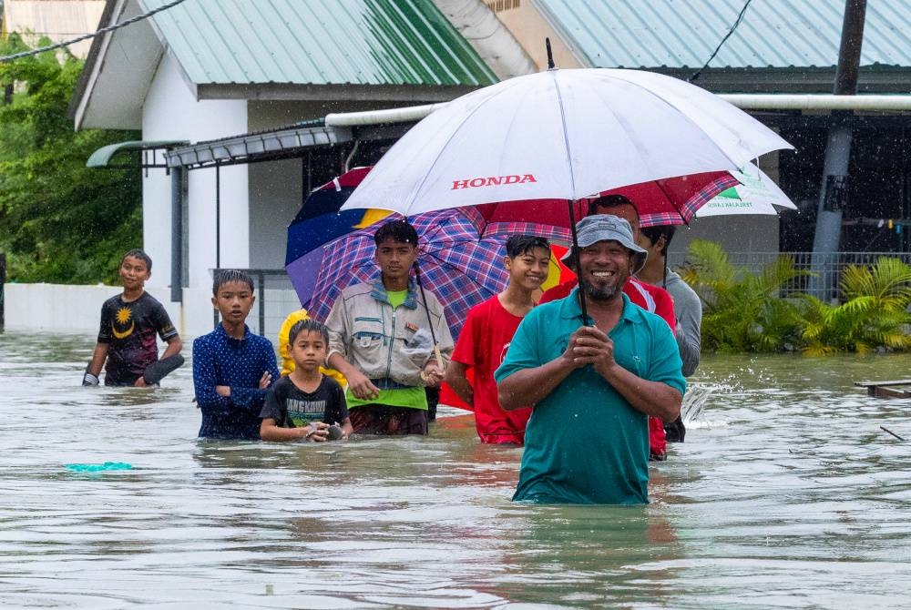 Beberapa penduduk Kampung Wakaf Stan meredah banjir untuk berpindah ke PPS yang berhampiran setelah rumah mereka dinaiki air berikutan hujan lebat sejak Sabtu lalu.   - Foto Bernama