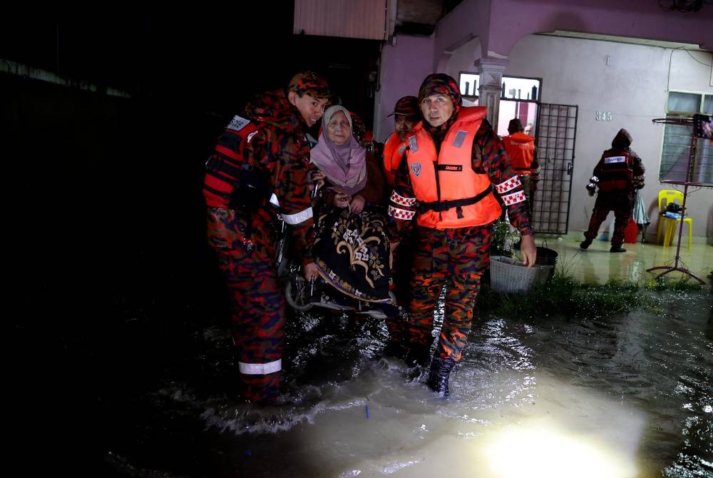 Anggota pasukan JBPM membantu menyelamatkan seorang pesakit strok yang terperangkap akibat banjir di Kampung Pulau Rusa Hulu malam tadi. - Foto Bernama