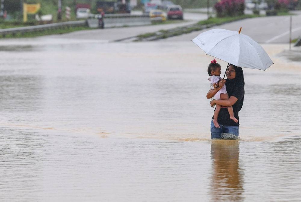 Seorang penduduk membawa anaknya meredah banjir untuk ke kawasan lebih selamat selepas kawasan itu dilanda banjir pada Selasa. - Foto Bernama