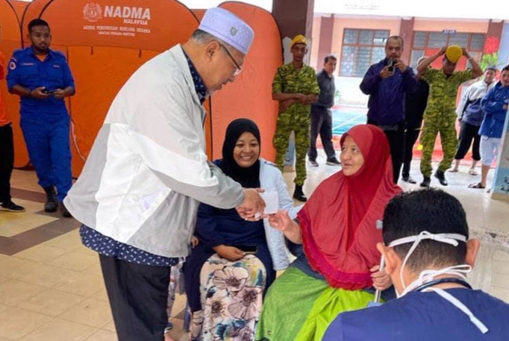 Ahmad (kiri) melawat mangsa banjir di pusat pemindahan sementara di Kutan, Tumpat.