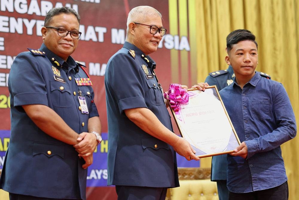 Mohammad Hamdan (tengah) menyampaikan sijil penghargaan JBPM kepada kepada Muhammad Zulfikal Asmadi, 14, (kanan) yang menyelamatkan seorang kanak-kanak hampir lemas di Pantai Penunjuk, Kijal, Terengganu, pada Jumaat lepas. - Foto Bernama