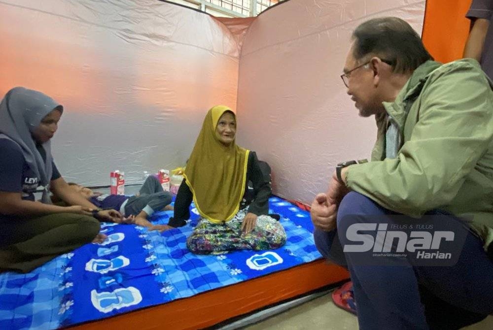 Anwar (kanan) bertanyakan khabar kepada mangsa banjir di PPS SMK Tengku Panglima Raja, Pasir Mas pada Rabu.