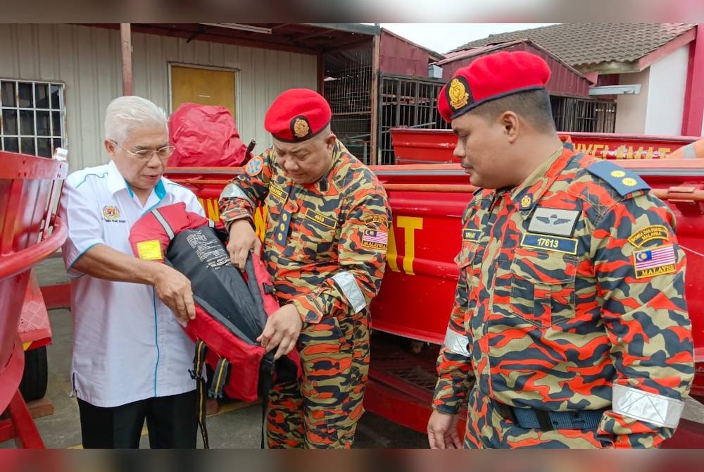 Ibrahim (tengah) menunjukkan kepada Hassan jaket keselamatan dan bot yang akan digunakan semasa menyelamatkan mangsa banjir, di BBP Pasir Gudang, pada Khamis.