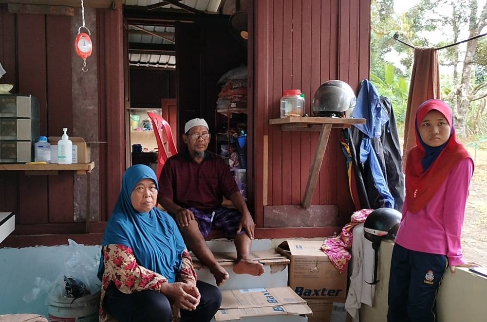 Hasan (dua dari kiri) bersama isteri dan anaknya yang menumpang teduh di sebuah stor kebun di Kampung Paya Rumput, Masjid Tanah pada Jumaat.