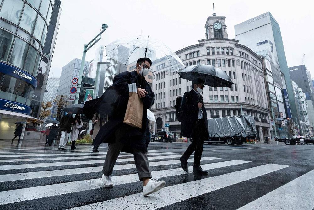 Orang ramai menyeberang jalan dalam cuaca sejuk dan hujan di kawasan Ginza di Tokyo pada Khamis. - Foto AFP