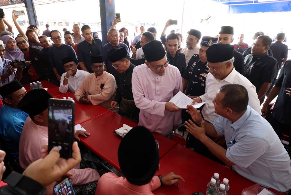 Anwar beramah mesra dengan pemilik gerai Sup Meletup Zolkhoari Abdul Aziz (kanan) sebelum menikmati makan tengah hari bersama pengunjung di gerai sup itu di Medan Selera Bandar Sri Permaisuri, Cheras, hari ini. - Foto Bernama