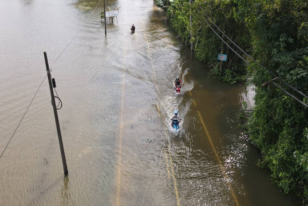 Penunggang motosikal meredah air banjir yang melimpahi jalan di Kampung Gelang Mas ketika tinjauan pada Jumaat. - Foto Bernama