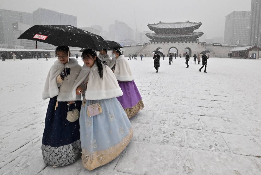 Pengunjung memakai pakaian tradisional bersiar-siar di Istana Gyeongbokgung semasa suhu paling sejuk melanda Seoul. - AFP