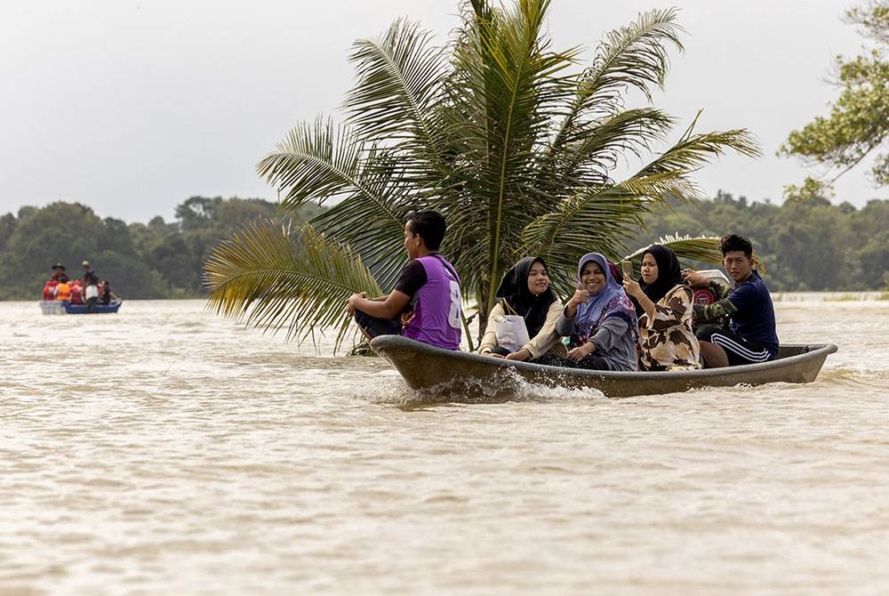 Sebahagian daripada penduduk Kampung Kubang Sawa menaiki sampan melalui kawasan bendeng padi yang menjadi seperti tasik buatan akibat banjir termenung di Kampung Telok Jering. -Foto Bernama