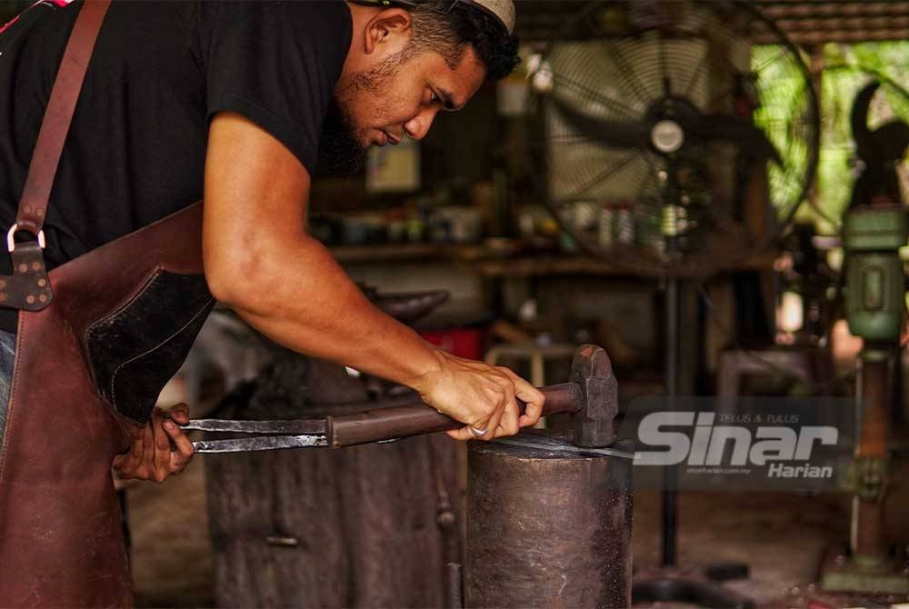 Muhammad Khairi Adham teliti ketika menempa dan menghasilkan parang di bengkel miliknya di Kampung Selendang dekat Padang Tengku, Lipis.