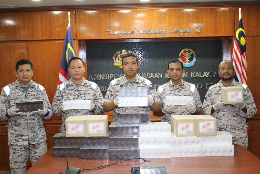 Nurul Hizam (tengah) menunjukkan rokok keretek yang dirampas Maritim Malaysia di perairan Pontian pada awal pagi Khamis.