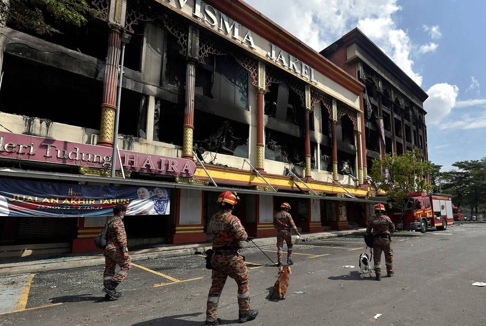 Anggota JBPM, Assan John (kanan) dan rakan Jovesster Junil (dua, kiri) membawa anjing pengesan Unit K9 Sam dan Rusty semasa melakukan siasatan kebakaran di Wisma Jakel, hari ini. Foto Bernama