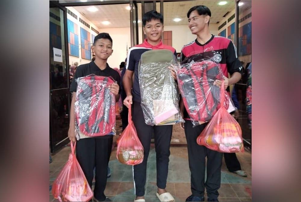 Tiga pelajar gembira menerima kit bantuan barangan keperluan persekolahan. - Foto UMT