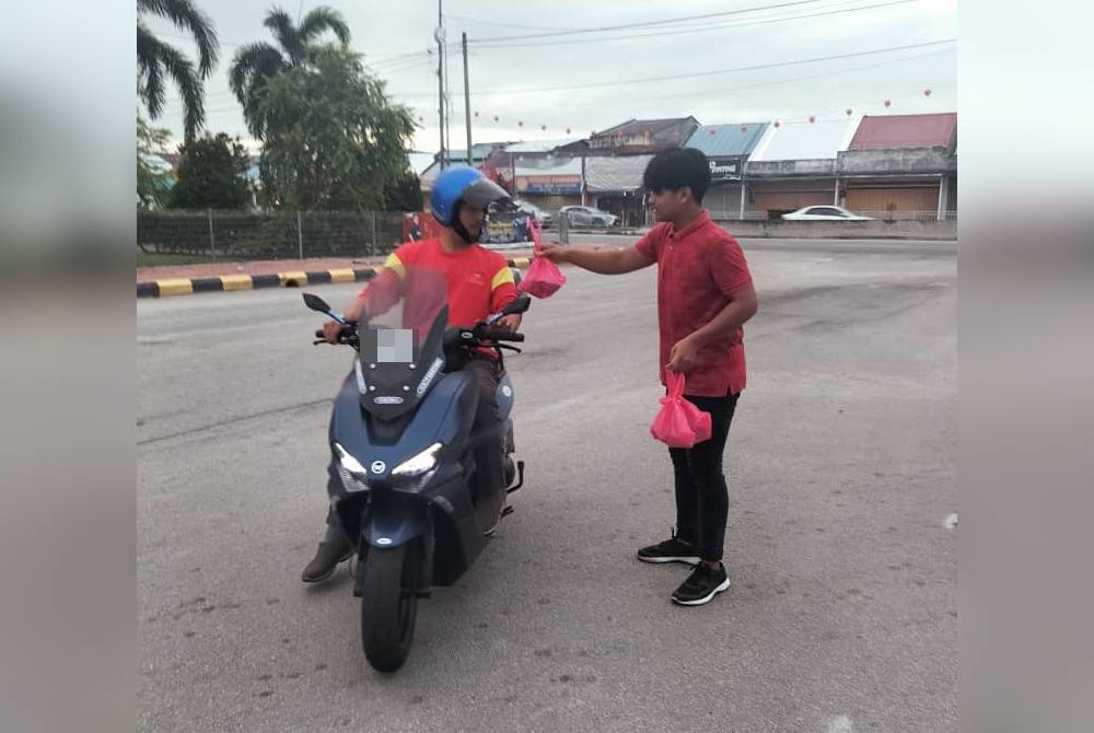 Izham Hakim (kanan) mengedarkan nasi lemak infak kepada orang ramai di Pekan Tanjong Karang.