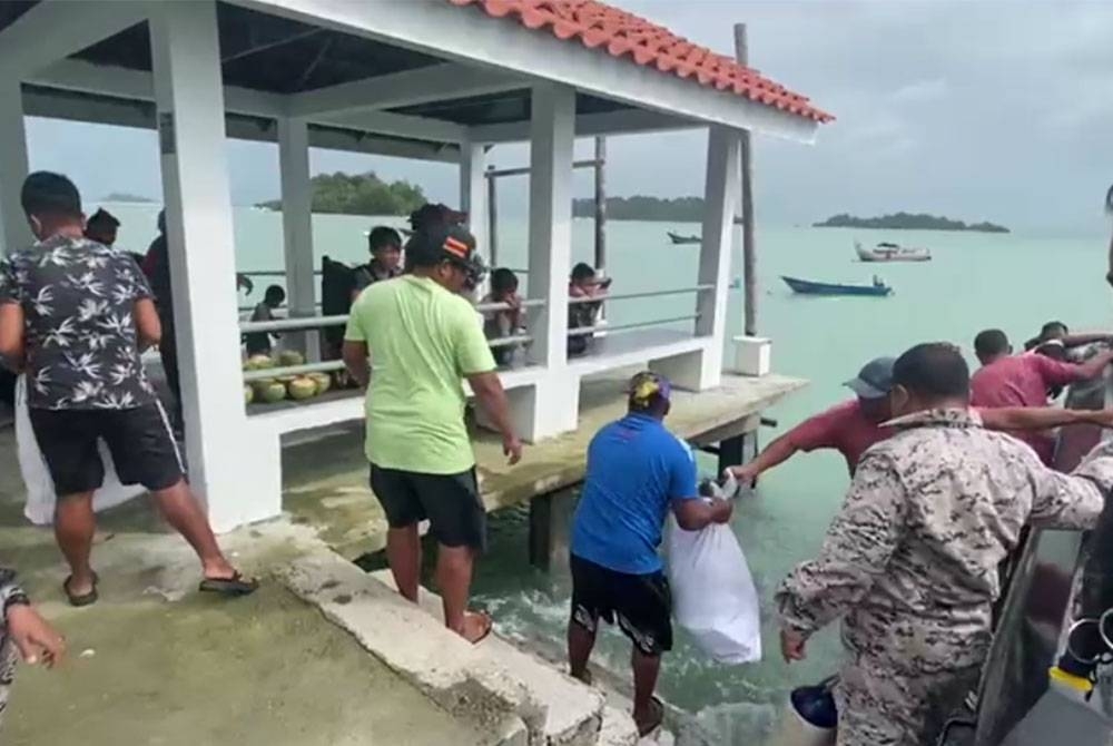 Anggota Maritim mengagihkan bantuan makanan kepada penduduk setempat sebaik tiba di jeti Pulau Tinggi pada Isnin.