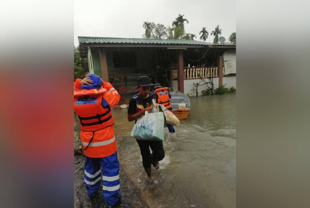 Anggota Angkatan Pertahanan Awam membantu memindahkan mangsa banjir dari Kampung Seri Damai ke PPS di dewan orang ramai kampung itu pada Isnin.