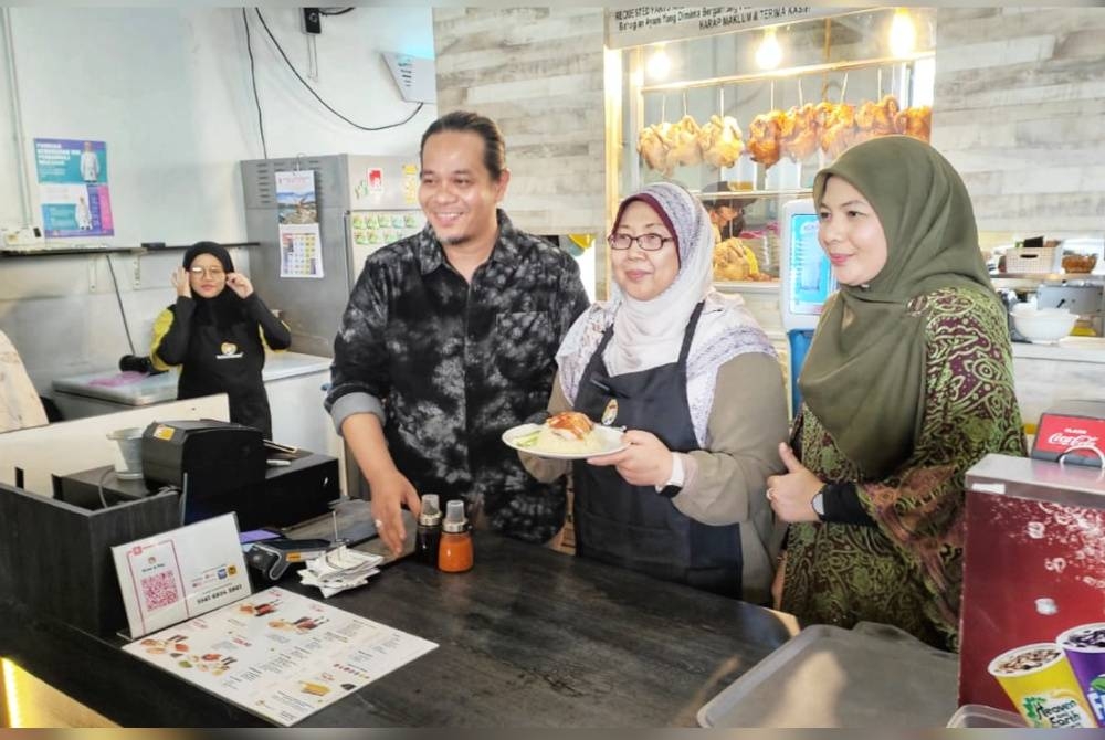 Fuziah (tengah) menunjukkan Menu Rahmah iaitu nasi ayam yang ditawarkan di restoran Nasi Ayam Papa di Indera Mahkota ketika mengadakan lawatan kerja pada Selasa.