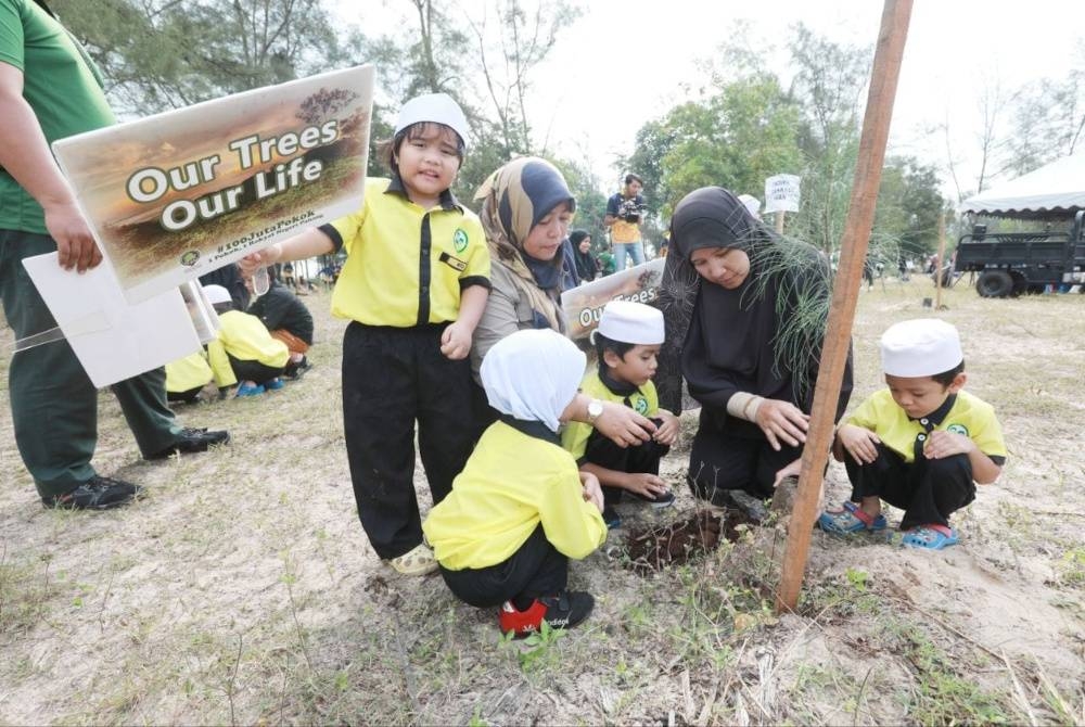 Nurfazliza (kiri) menanam pokok ru pantai bersama kanak-kanak di Kambung Kempadang.