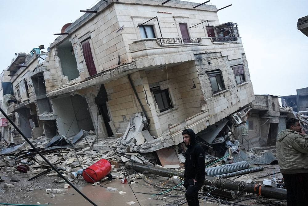 Seorang penduduk berdiri di depan bangunan runtuh akibat gempa bumi berlaku di bandar Jandaris di wilayah Aleppo, Syria. - AFP