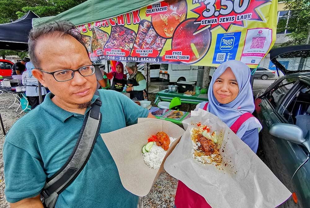 Hasriah (kanan) dan Nik Syamsudin menunjukkan hidangan nasi berlauk yang dijual pada harga RM3.50.