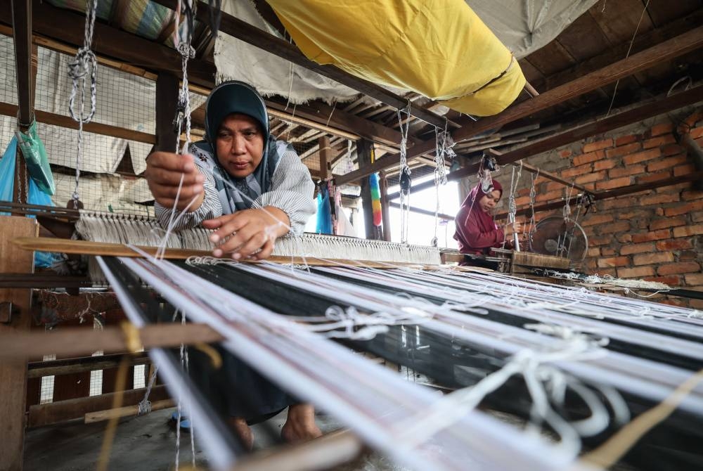 Gayah Awang, 54, sedang sibuk menenun kain di rumahnya di Kampung Pasir Panjang. - Foto Bernama