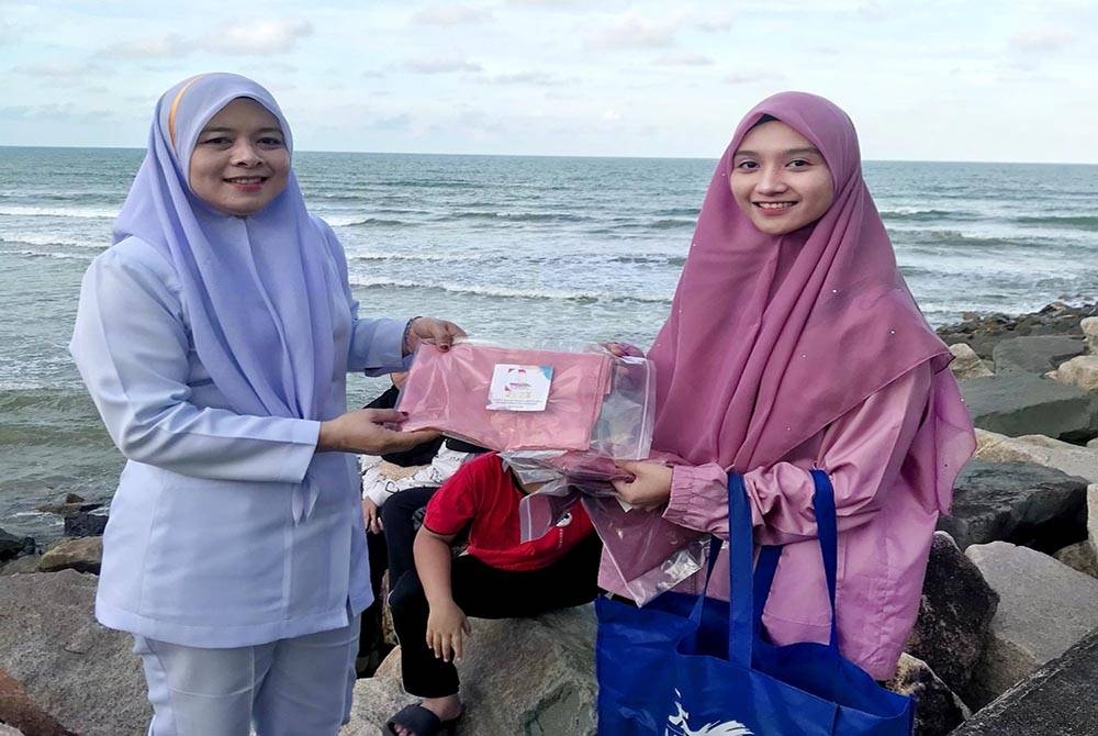 Hanim Sophia (kanan) ketika menyerahkan tudung percuma di sekitar Pantai Pulau Kekabu di Marang.