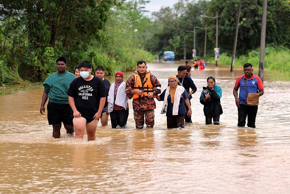 Seorang anggota Jabatan Bomba dan Penyelamat Malaysia (JBPM) membantu orang ramai meredah banjir di laluan utama ke Kampung Kelantan di Kota Tinggi pada Rabu. - Foto Bernama