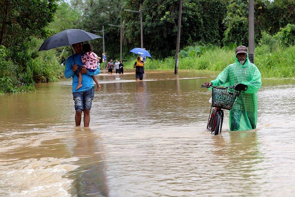 Orang ramai meredah banjir di laluan utama ke Kampung Kelantan di Kota Tinggi pada Rabu. - Foto Bernama