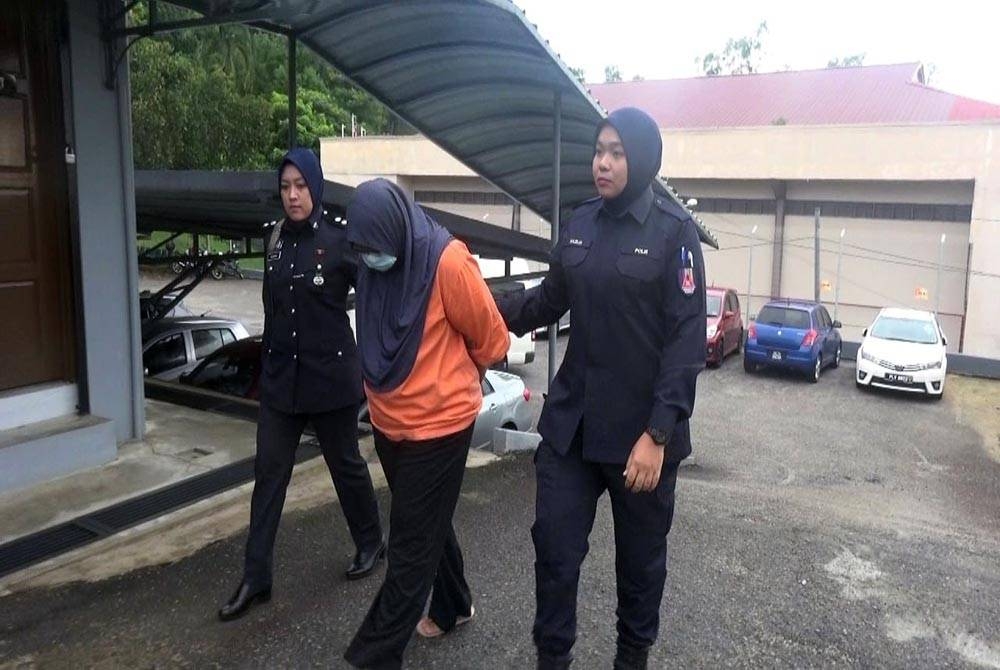 Tertuduh (tengah) diiringi pegawai polis sebaik tiba di perkarangan mahkamah pada Khamis.