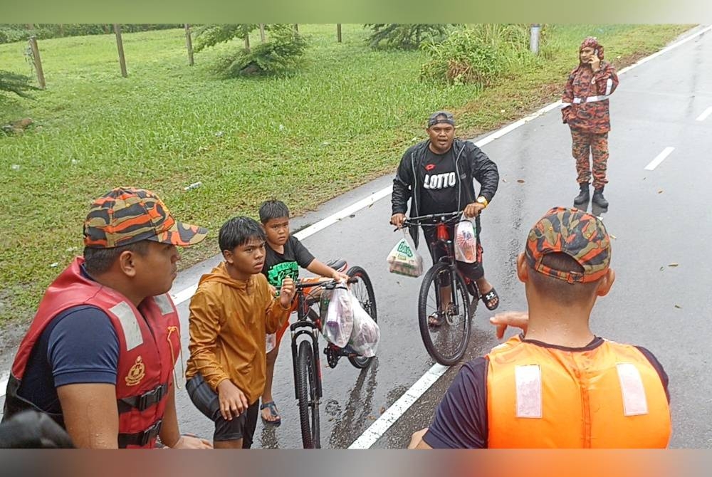 Junaidi (dua dari kanan) bersama dua anaknya menaiki basikal untuk membeli makanan dibantu anggota bomba untuk pulang ke rumah mereka di Kampung Tembioh Kota Tinggi pada Jumaat.