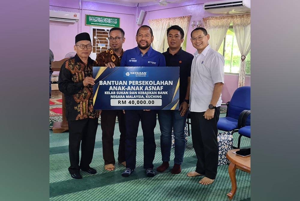 Syaiful Rizal (tengah) menyerahkan simbolik replika cek bantuan persekolahan kepada wakil penerima di Masjid Darul Rahmah Tambirat, Kuching pada Sabtu.