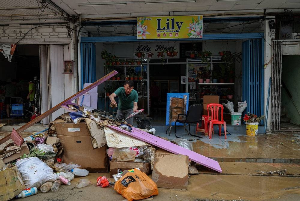 Pemilik sebuah premis perniagaan melakukan kerja-kerja pembersihan selepas banjir mulai surut di sekitar Jalan Dato Sia Her Yam, Bandar seberang pada Ahad. - Foto Bernama