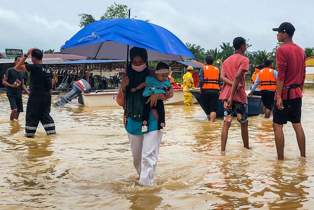 Mangsa banjir mengendong anak kecilnya selepas keluar dari Kampung Parit Warijo, Sri Medan, Batu Pahat yang dinaiki air ketika tinjauan pada Sabtu. - Foto Bernama