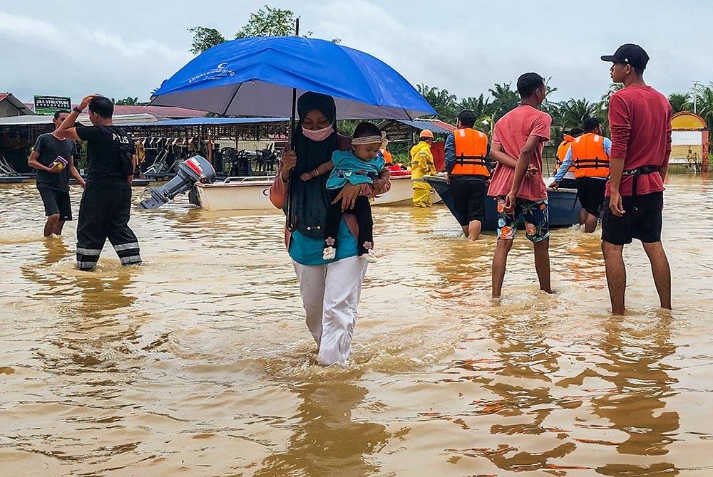 Mangsa banjir mengendong anak kecilnya selepas keluar dari Kampung Parit Warijo, Sri Medan, Batu Pahat yang dinaiki air ketika tinjauan pada Sabtu. - Foto Bernama