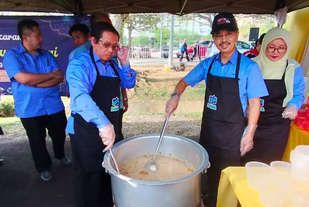 Abdul Rashid (kanan) mengagihkan bubur lambuk kepada pengunjung Pasar Tani Putrajaya.