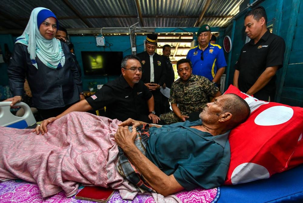 Adly (dua dari kiri) melawat Che Ahmad yang terlantar akibat komplikasi usus pada Jelajah Program Peduli Veteran ATM di Kampung Pulau Panjang, Pengkalan Chepa hari ini. - Foto Bernama