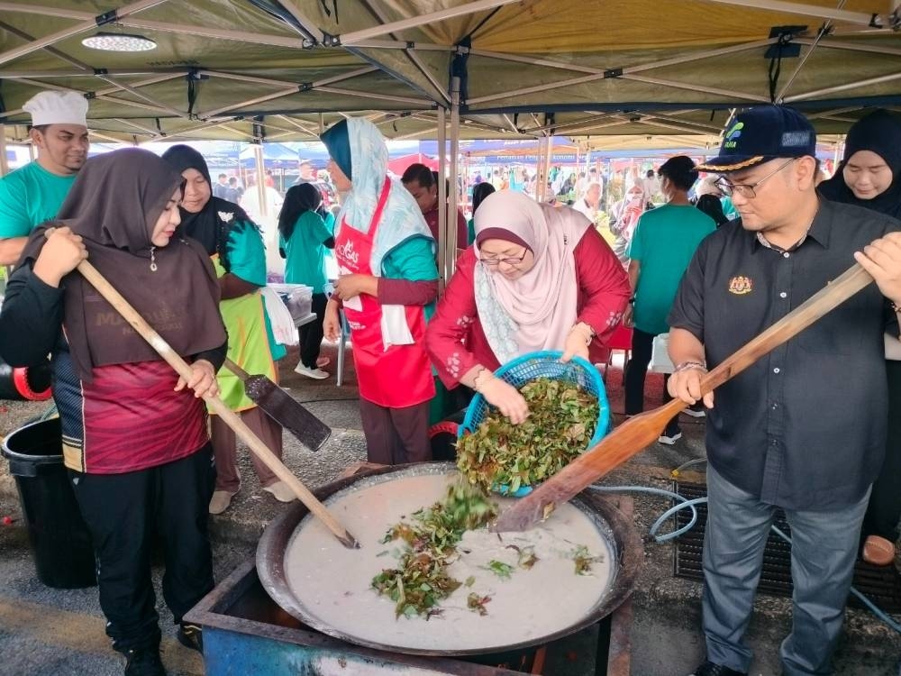 Fuziah (tengah) membantu memasukkan sayuran di dalam bubur lambuk sempena Ramadan di Pasar Tani UTC di sini pada Ahad.