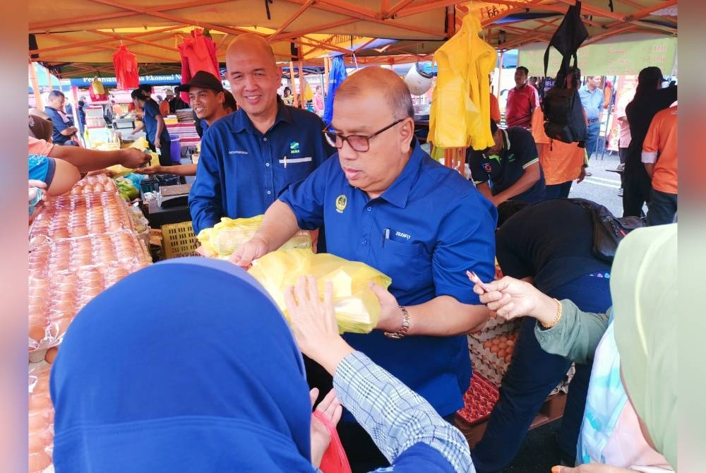 Mohd Zolkafly (kanan) bersama Noorsham membantu jualan sesi Happy Hour bagi telur yang dijual RM10 sepapan sempena pelancaran Jualan Ramadan Madani di Pasar Tani Tapah pada Selasa.
