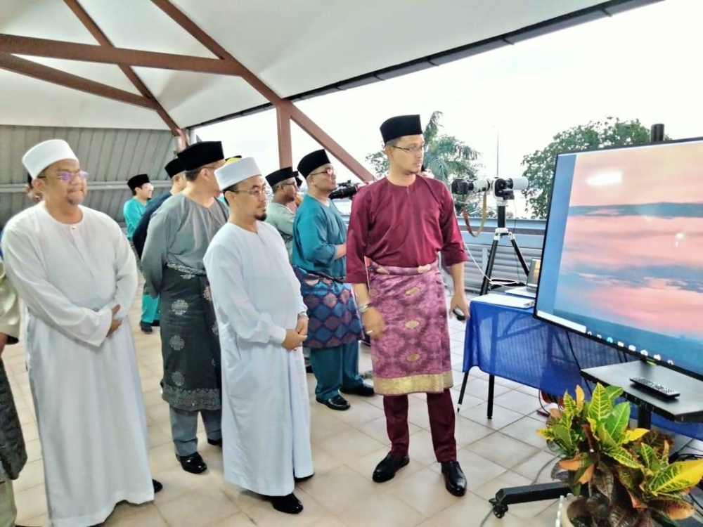 Mohd Fared (kanan) melihat proses cerapan anak bulan Ramadan di Pontian pada petang Rabu.