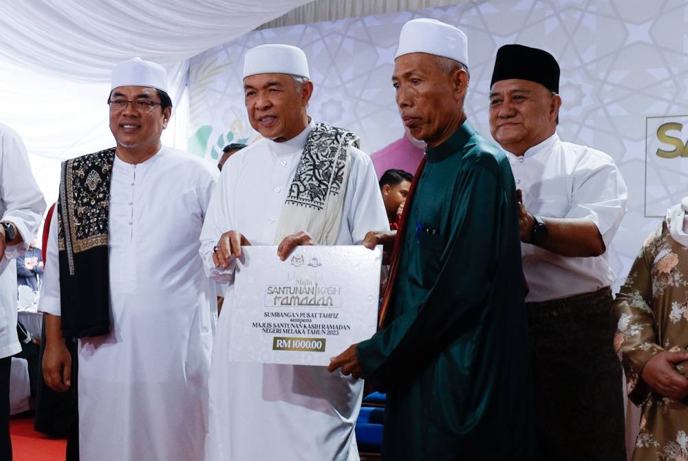 Ahmad Zahid (dua dari kiri) menyampaikan sumbangan Sekolah Tahfiz kepada wakil dari Sekolah Pondok dan Tahfiz Tuan Guru Haji Husin, Supriyadi Sage pada Majlis Santunan Kasih Ramadan di Masjid Jamek Ar-Rahman Kampung Pulai dekat Serkam, pada Isnin. - Foto Bernama