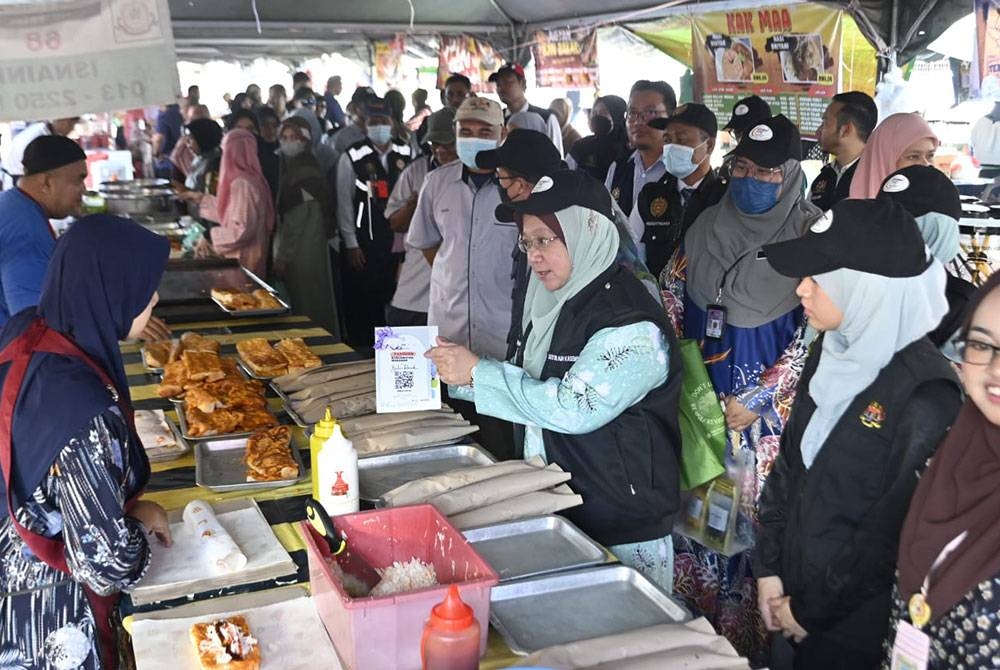 Dr Kasemani memberi penerangan mengenai kod imbasan QR yang ditempatkan di bazar Ramadan kepada peniaga ketika melawat bazar Ramadan Gong Badak, Kuala Nerus.