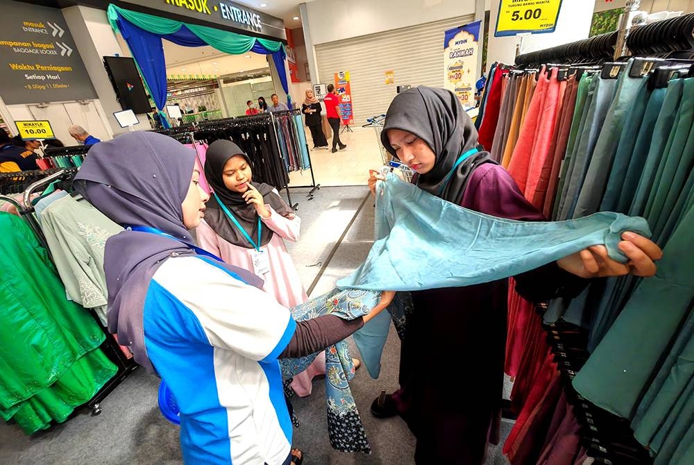 Nur Qaseeh Nasuha (kanan) memilih tudung raya sambil dibantu kakitangan SWM Sdn Bhd.