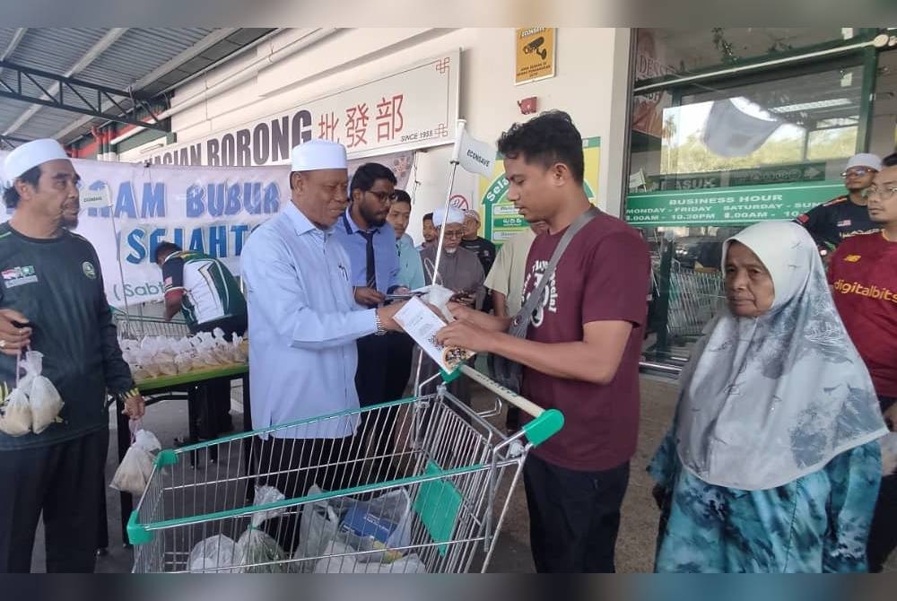 Wan Romani (dua dari kanan) agih sebanyak 1,500 bungkus bubur lambuk pada Program Bubur Lambuk Sejahtera di pasar raya Econsave cawangan Pokok Sena pada petang Sabtu.