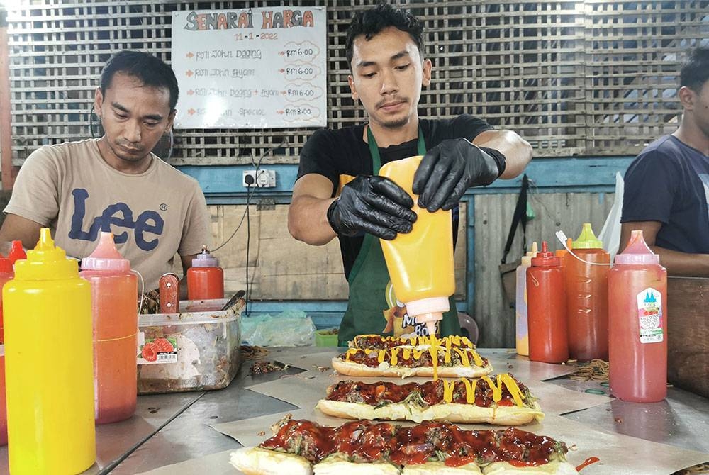 Pekerja menyediakan roti john yang ditempah pelanggan.