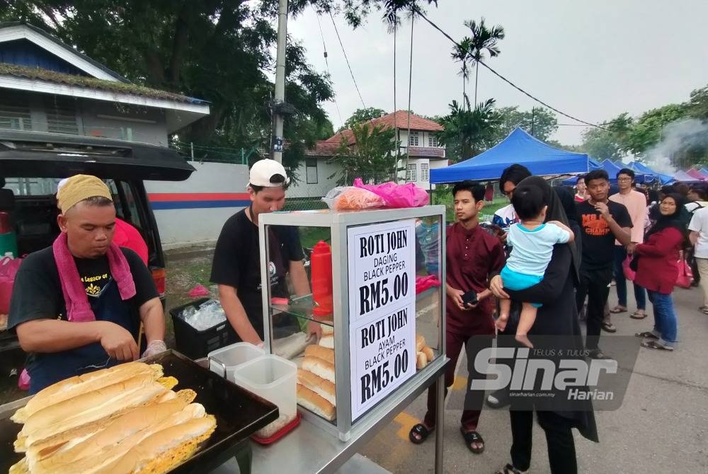 Orang ramai sanggup beratur panjang untuk membeli roti john di gerai Muhammad Tarmizi (kiri) di Bazar Ramadan Peringgit.