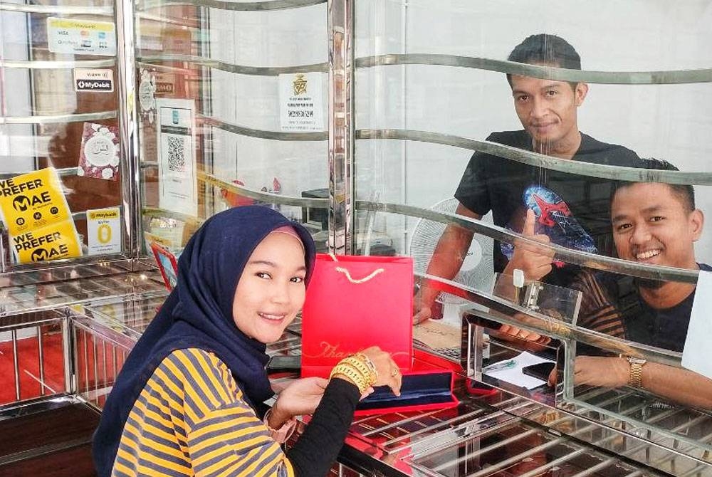 Muhammad Ismail (kanan, duduk) ketika melayani seorang pelanggannya di Kedai Emas Pilah.