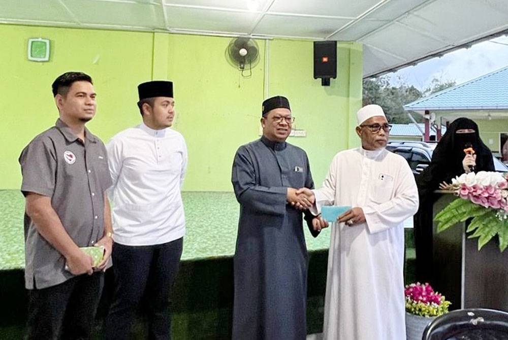 Zuhairi (tiga dari kiri) menyampaikan sumbangan duit raya pada majlis berbuka puasa bersama anak yatim dan warga emas di Madrasah Kamaliah Kampung Cherok Paloh di sini