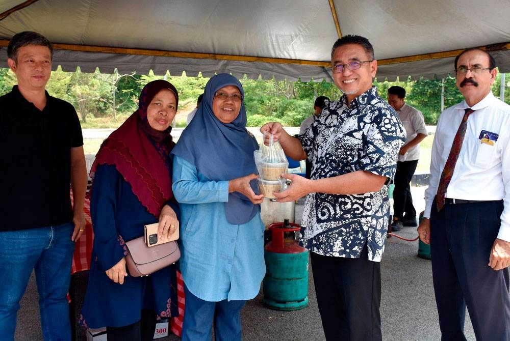 Adly (dua, kanan) mengagihkan bubur lambuk kepada pengunjung. - Foto Bernama